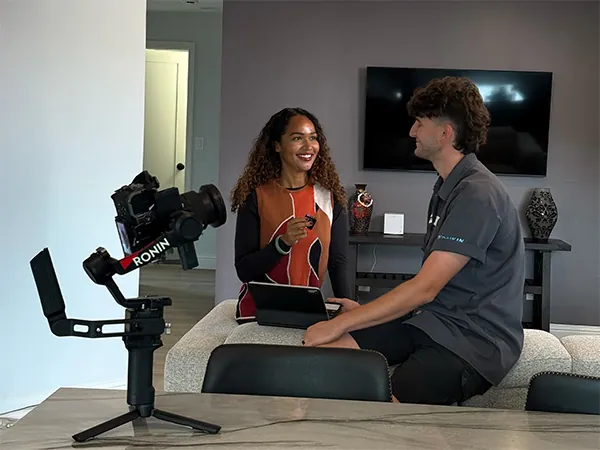 Two people talking on a couch, with a camera on a gimbal in the foreground.
